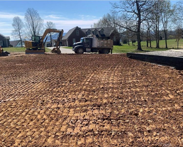Residential Land Grading and Site Preparation in Knoxville A freshly graded residential lot with visible tire tracks, featuring a skid steer and excavator on-site near new homes under construction.